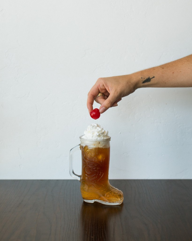Root beer espresso tonic with whipped cream in a boot-shaped glass